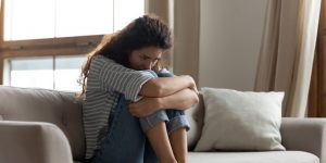Woman sitting on a couch, hugging her knees, appearing contemplative and distressed, reflecting themes of depression and emotional support.