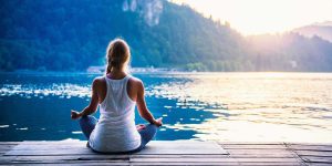 Woman meditating by serene lake at sunset, reflecting mindfulness and healing practices related to trauma recovery.