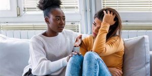 Two women sitting on a couch, one comforting the other, discussing emotional support and coping with depression.