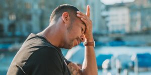 Man with a pained expression holding his forehead, reflecting emotional distress related to depression and mental health challenges.