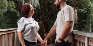 Couple holding hands on a wooden bridge, smiling and engaging in a moment of connection, symbolizing trust and communication in relationships.