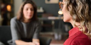 Two women engaged in a counseling session, one speaking and the other listening attentively, reflecting trauma recovery and emotional support themes.