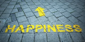 Yellow arrow pointing upwards with the word "HAPPINESS" painted on a stone pavement, symbolizing a positive journey towards mental well-being and recovery from depression.