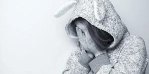 Young woman in a bunny hoodie covering her face, conveying emotions of distress or sadness, relevant to mental health discussions and support resources.
